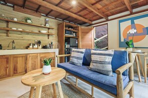 A modern kitchen with wooden cabinets, a built-in oven, and a dining area with a blue sofa and wooden table. - Sakara Bali Villa by Kozystay - Ubud (Kabupaten Gianyar)