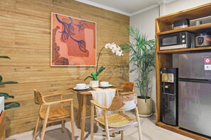 A dining area with a wooden table, chairs, a decorative painting, and a refrigerator. - Sakara Bali Villa by Kozystay - Ubud (Kabupaten Gianyar)