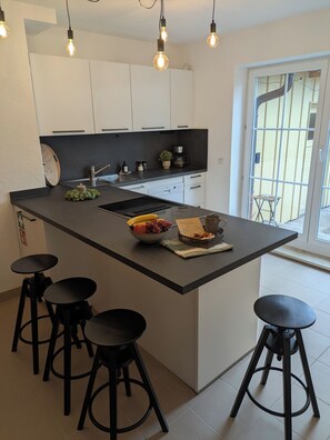 A modern kitchen with a central island, black stools, and pendant lighting. - 100-square-meter vacation rental with 3 separate bedrooms (Ruhpolding)
