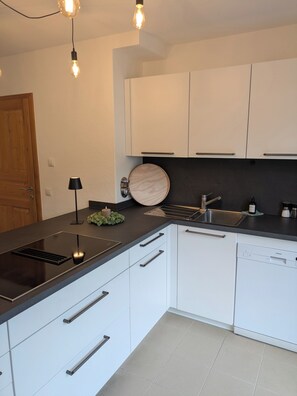 A modern kitchen with white cabinets, a black countertop, and a built-in dishwasher. - 100-square-meter vacation rental with 3 separate bedrooms (Ruhpolding)