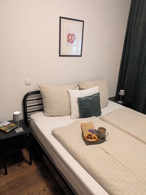 A hotel room with a bed, pillows, a bedside table with a lamp, a framed picture on the wall, and a tray with pretzels and a cup. - 100-square-meter vacation rental with 3 separate bedrooms (Ruhpolding)