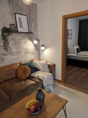 A living room with a brown leather sofa, a wooden coffee table with fruit, a wall-mounted light fixture, and a framed picture. - 100-square-meter vacation rental with 3 separate bedrooms (Ruhpolding)