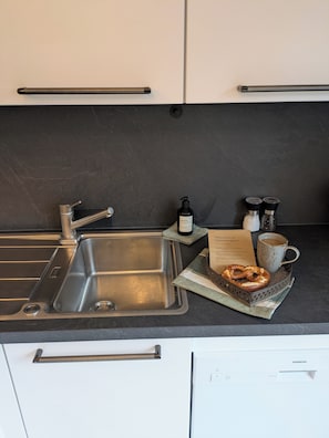 A kitchen with a stainless steel sink, a coffee maker, a bottle of hand soap, salt and pepper shakers, and a tray with a pretzel. - 100-square-meter vacation rental with 3 separate bedrooms (Ruhpolding)