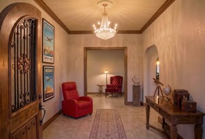 Ein Flur mit einer Chandelier, einem roten Sessel, einem Holztisch mit Globus und gerahmten Postern an der Wand.