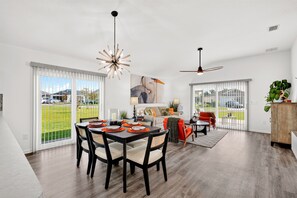 A spacious dining area with a large table and chairs, a ceiling fan, and a view of the outdoors through large windows.