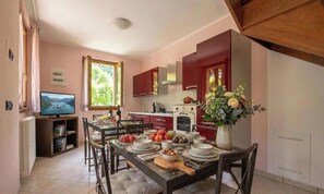 A dining area with a table set for four, a television, and a kitchen in the background. - NEW LarioView Suites – Lake View Apartment with Terrace in Argegno (Argegno)