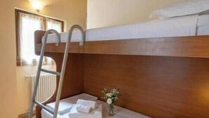 Uma cama beliche com escada, uma pequena mesa de cabeceira com um vaso e uma janela com cortinas.