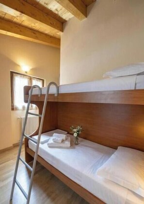 A bunk bed with a ladder, a small bedside table with a vase, and a window with curtains. - NEW LarioView Suites – Lake View Apartment with Terrace in Argegno (Argegno)