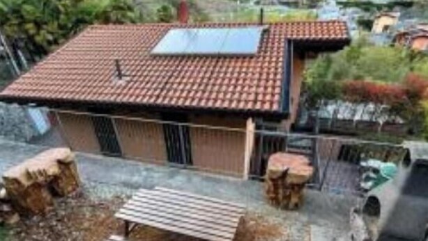 Uma casa com telhado de telhas, um banco de madeira e um painel solar.