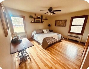 Ein Schlafzimmer mit einem Bett, einer Nähmaschine, einem Deckenventilator und einem Fenster.