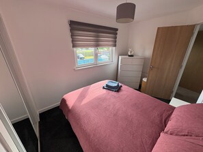 A bedroom with a bed, a dresser, a window with blinds, and a door. - Under 10m to Airport/Hospital/Hydro/Breahead/City (Renfrew)