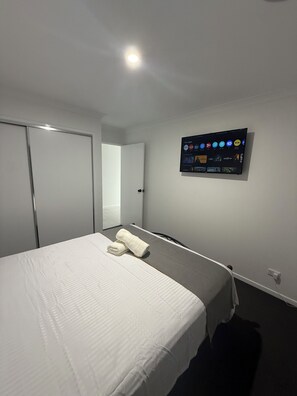 Una camera d'albergo con un letto, una TV a muro che mostra diverse app, una porta chiusa e una presa elettrica sulla parete.