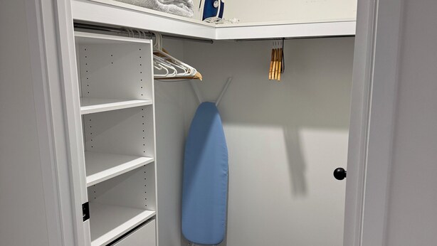En garderob med hyllor, en klädstång och en strykbräda.