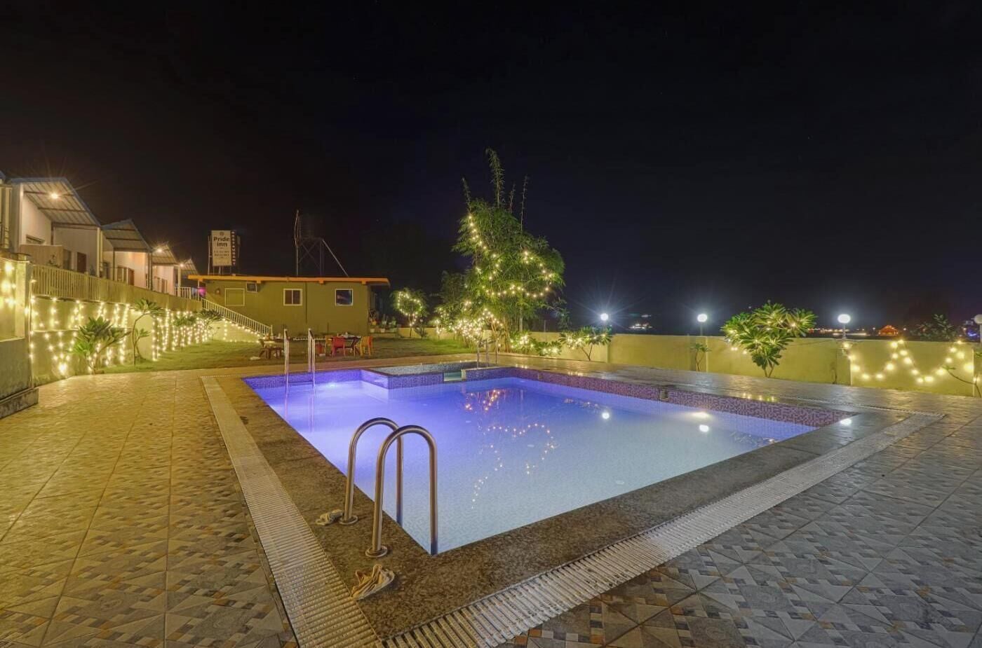 Una piscina con borde de baldosas, rodeada por un muro bajo con luces colgantes.