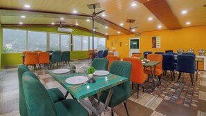 A dining area with tables and chairs, a ceiling fan, and a view through large windows. - PrideInn Luxury Resort (Simal Khet)