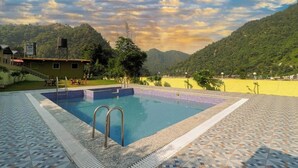 A swimming pool with a tiled deck, surrounded by a mountainous landscape and a building with a sign. - PrideInn Luxury Resort (Simal Khet)