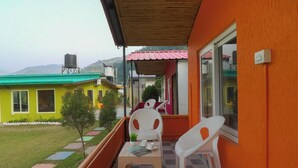 A balcony with a table and chairs, a view of a green lawn, and colorful buildings in the background. - PrideInn Luxury Resort (Simal Khet)