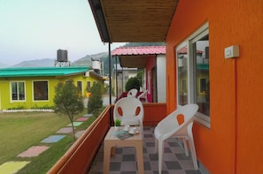 Uma varanda com mesa e cadeiras, vista para um gramado verde e edifícios coloridos ao fundo.