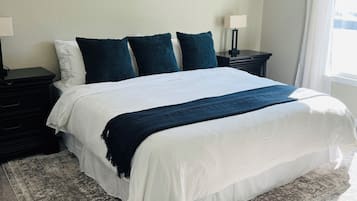 Un dormitorio con cama, mesita de noche, lámpara, ventilador de techo y ventana con cortinas.