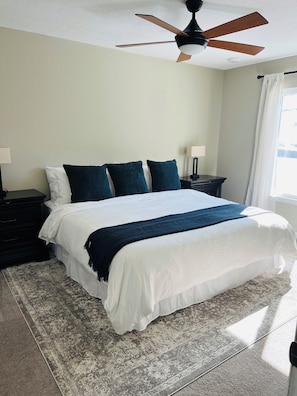 A bedroom with a bed, a nightstand, a lamp, a ceiling fan, and a window with curtains.