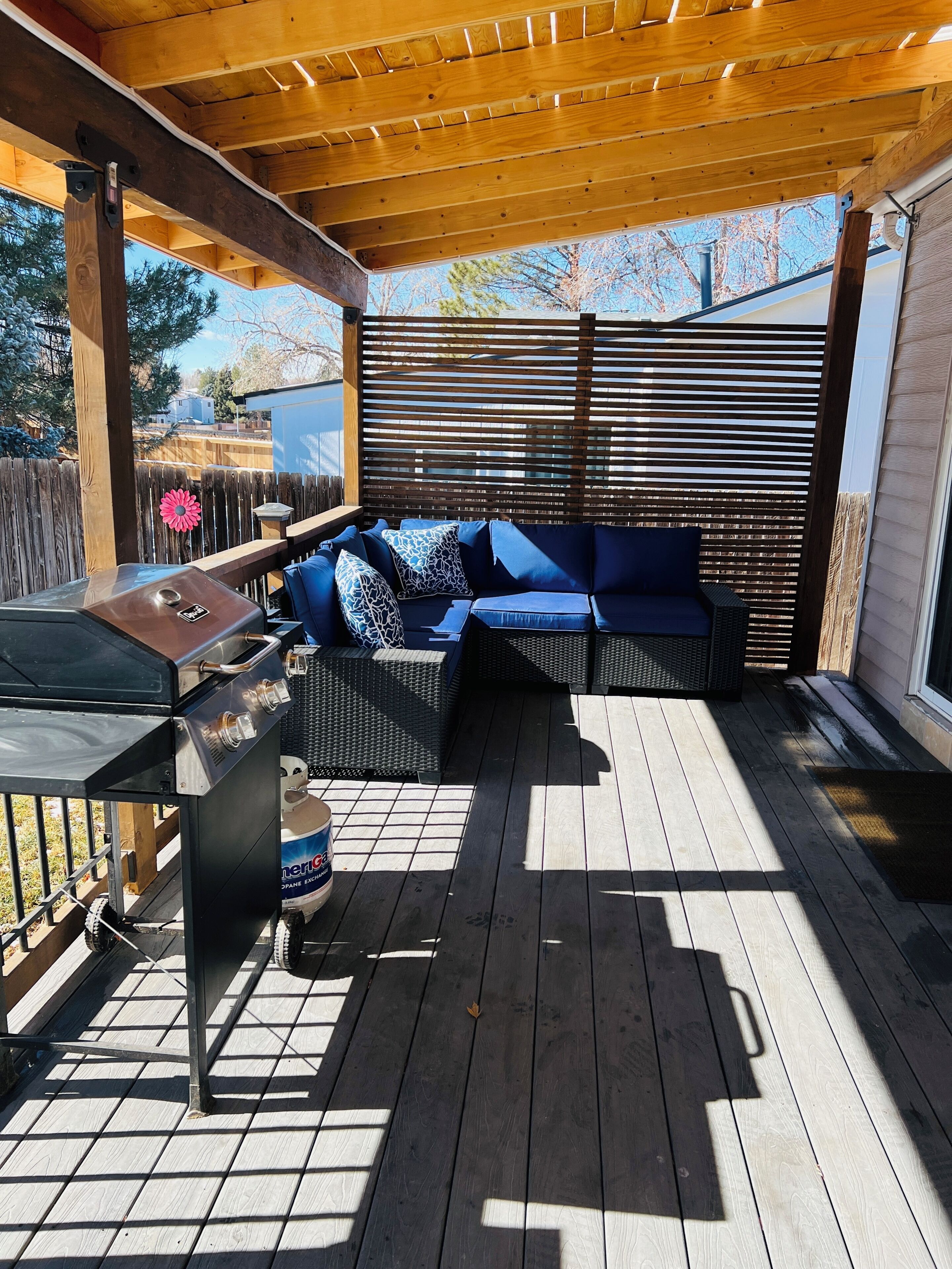 An outdoor patio with a grill, seating area, and wooden deck.