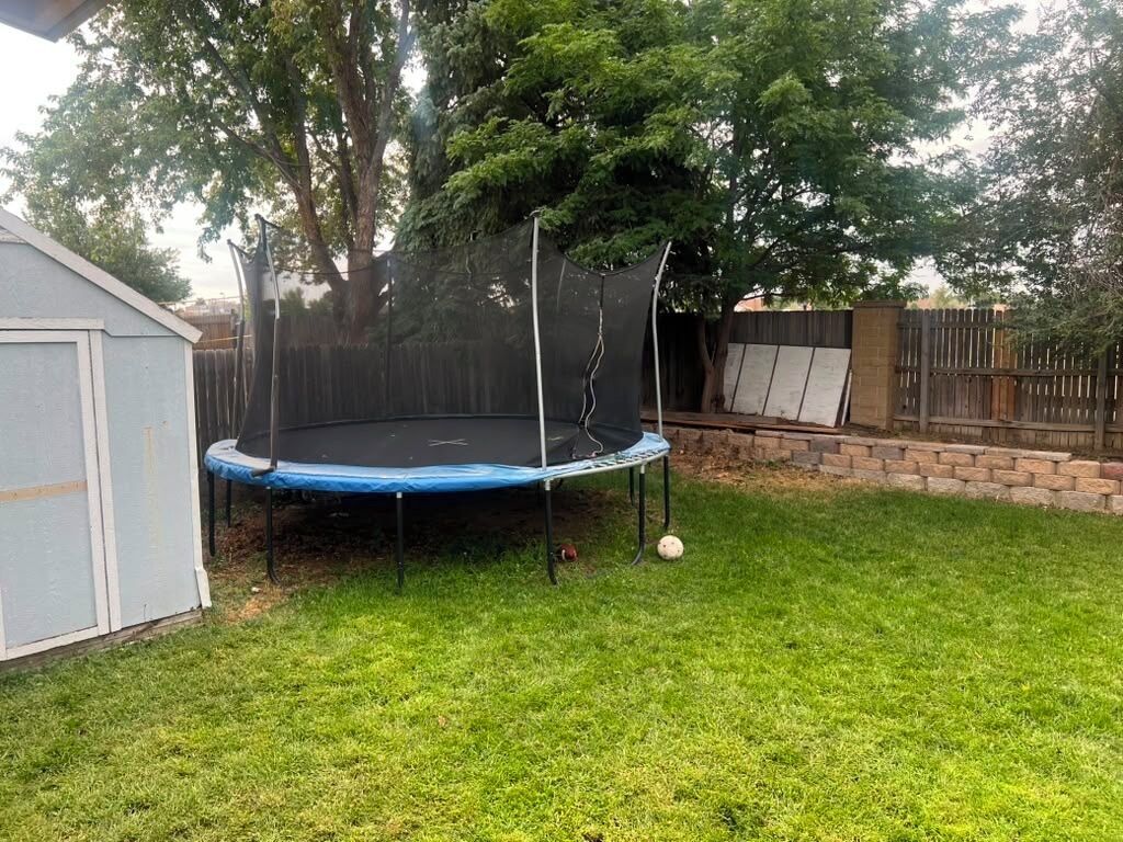Un patio trasero con un trampolín, un cobertizo y una valla de madera.