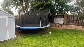 Un patio trasero con un trampolín, un cobertizo y una valla de madera.