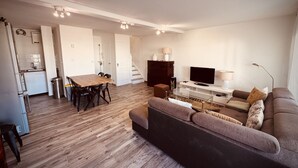 A modern apartment with a dining area, a sofa, a TV, and a staircase. - The Pink Hippopotamus – Duplex with a terrace overlooking the M (Sète)