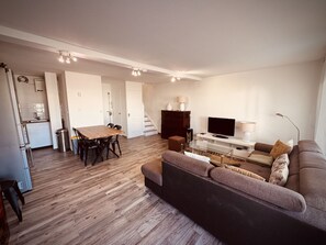 A modern apartment with a dining area, a sofa, a TV, and a staircase. - The Pink Hippopotamus – Duplex with a terrace overlooking the M (Sète)