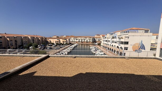 A marina with boats docked, a building with a sailboat logo, and a clear sky. - The Pink Hippopotamus – Duplex with a terrace overlooking the M (Sète)