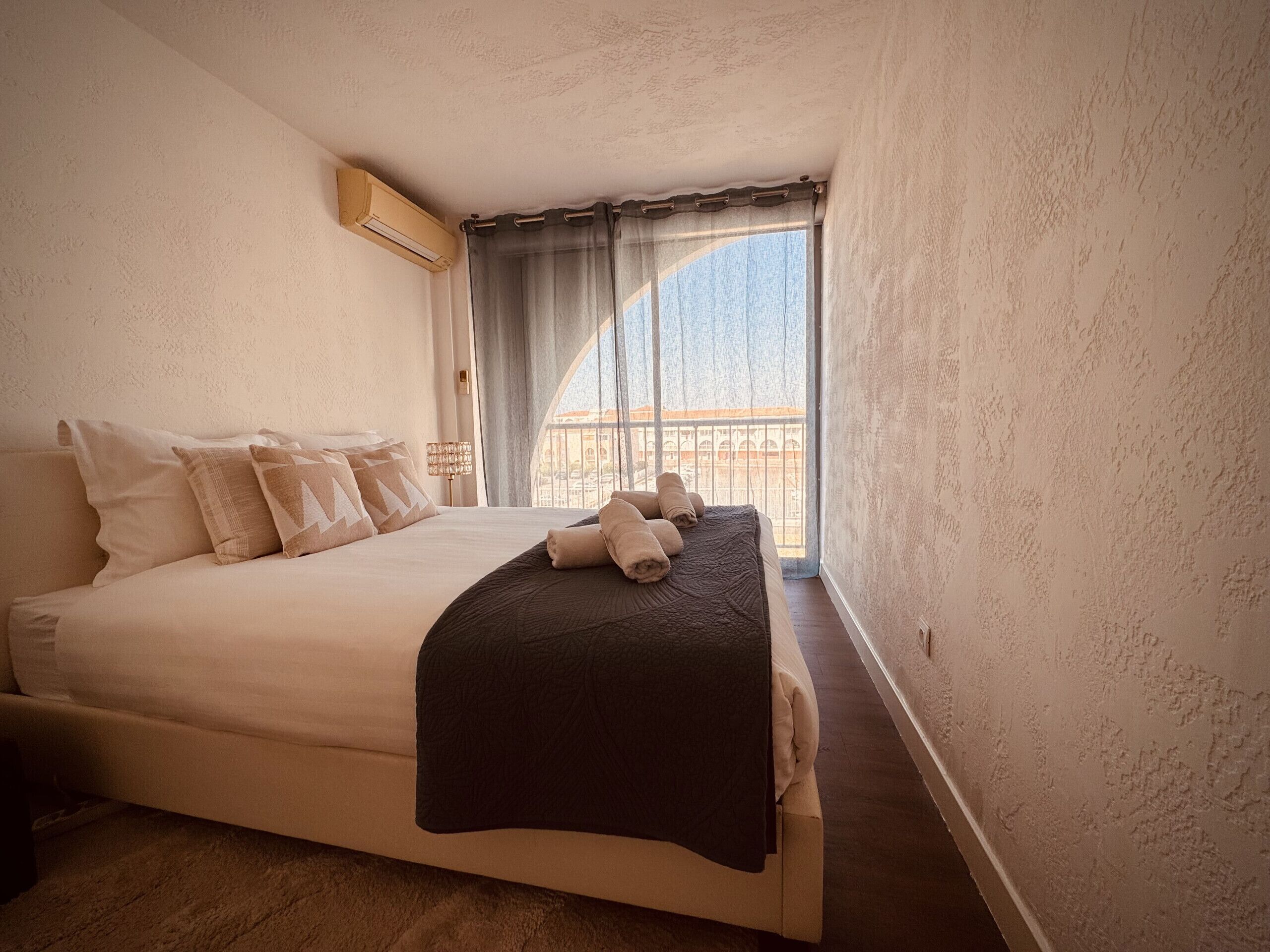 Une chambre à coucher avec un lit, des oreillers, une couverture, une fenêtre avec des rideaux et un appareil de climatisation.