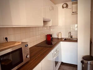 A modern kitchen with white cabinets, a microwave, a coffee maker, and a dishwasher. - The Pink Hippopotamus – Duplex with a terrace overlooking the M (Sète)