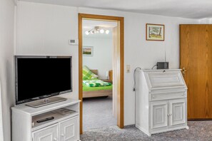 A hotel room with a television, a small cabinet, a bed with a green and white striped blanket, a wooden door, and a small table with a radio.