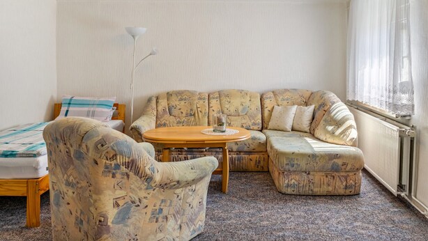 Una habitación con sofá, sillón y una pequeña mesa con un florero de vidrio.