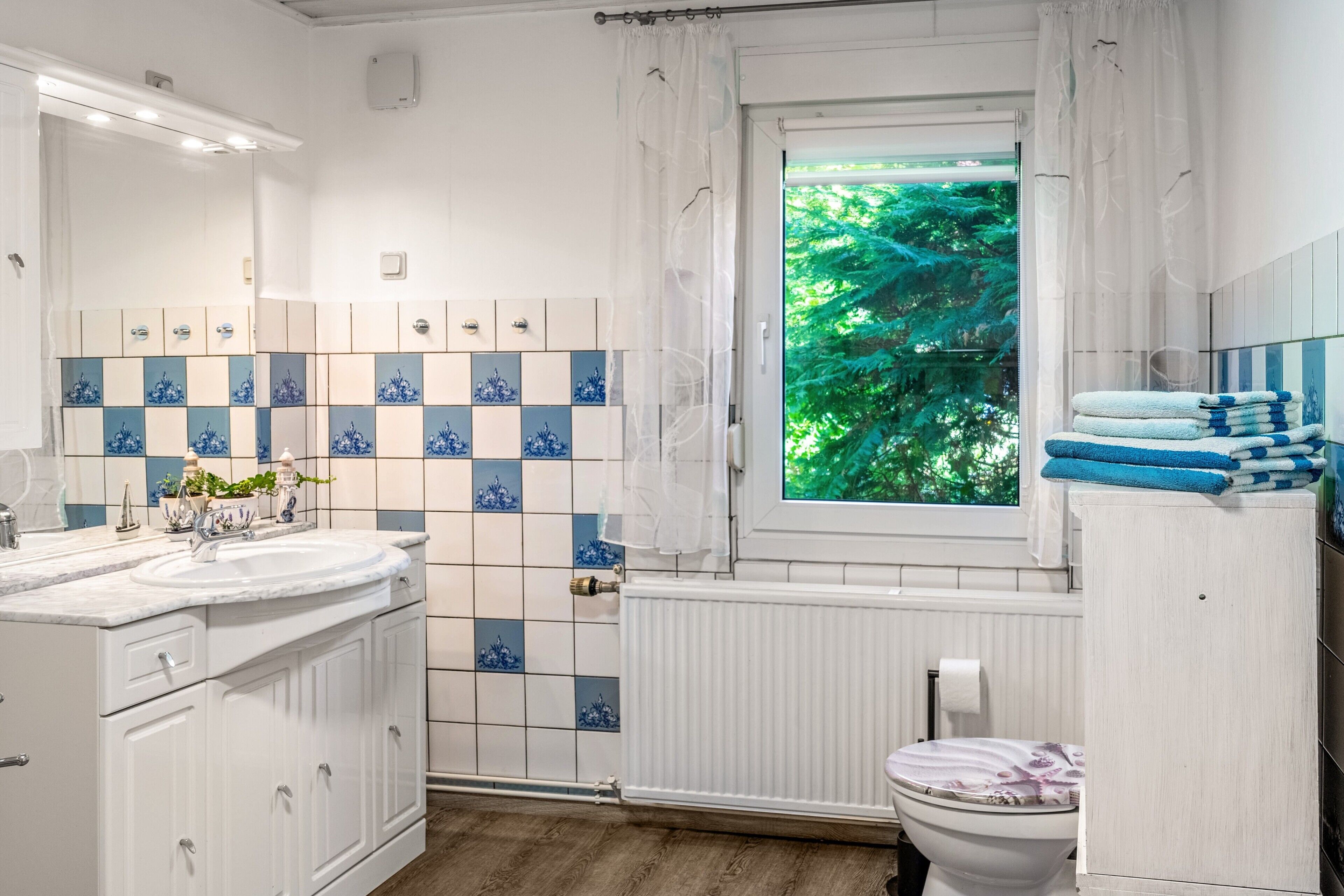 A bathroom with a white sink, vanity, and a window with a view of greenery.