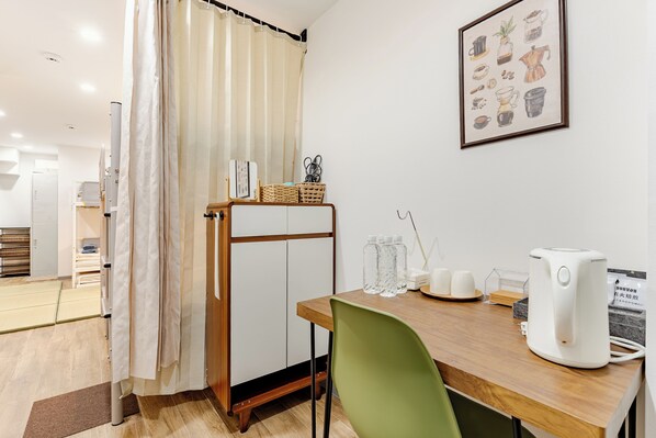 A compact room with a wooden table, a green chair, a white kettle, and a framed picture on the wall.