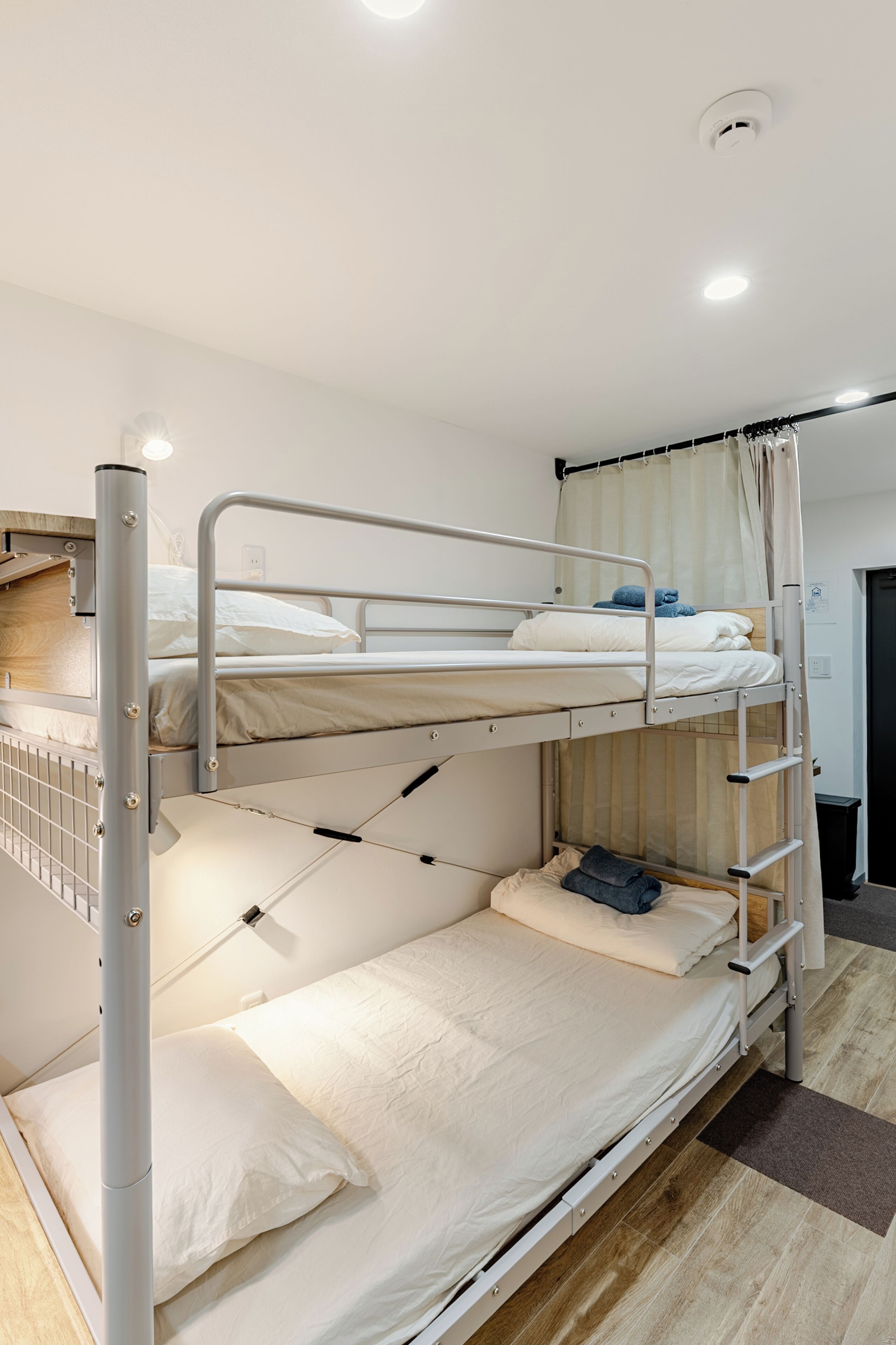 A bunk bed with a pull-out desk, a window with curtains, and a door to the right.