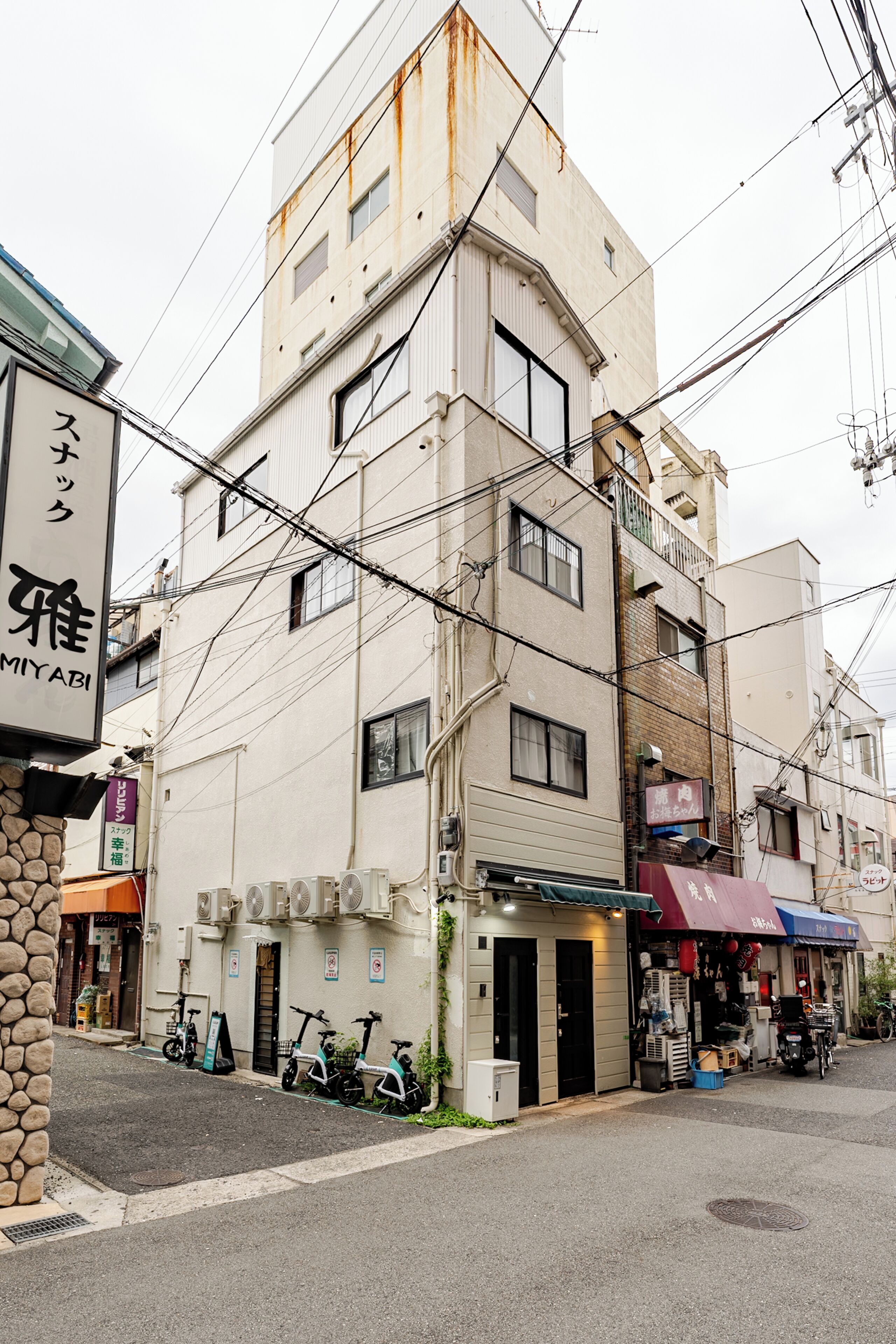 A multi-story building with a ground-level commercial space, a visible entrance, and a row of parked scooters.