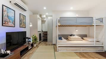 A compact hotel room with a bunk bed, a flat-screen TV, a small kitchenette, and a painting on the wall.