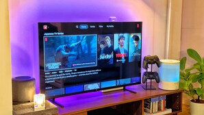 Un téléviseur à écran plat posé sur un meuble en bois, avec une manette de jeu et une plante en pot à côté.