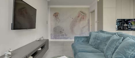 A modern living room with a grey sofa, a flat-screen TV, and a glass coffee table with a magazine.