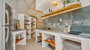 Eine kompakte Küche mit integriertem Kühlschrank, Mikrowelle und Herd. Holzregale und eine Arbeitsplatte mit verschiedenen Küchenutensilien.