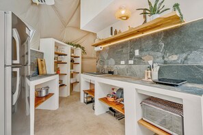 Eine kompakte Küche mit integriertem Kühlschrank, Mikrowelle und Herd. Holzregale und eine Arbeitsplatte mit verschiedenen Küchenutensilien.