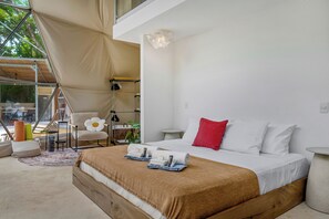 A modern bedroom with a large bed, a chair, a small table, and a hanging light fixture. - Private Domes with a Pool Near Playa Grande (Matapalo)