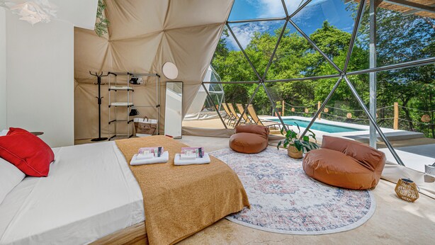 Ein Zeltraum mit Bett, Handtüchern, einem Spiegel und Blick auf einen Swimmingpool.