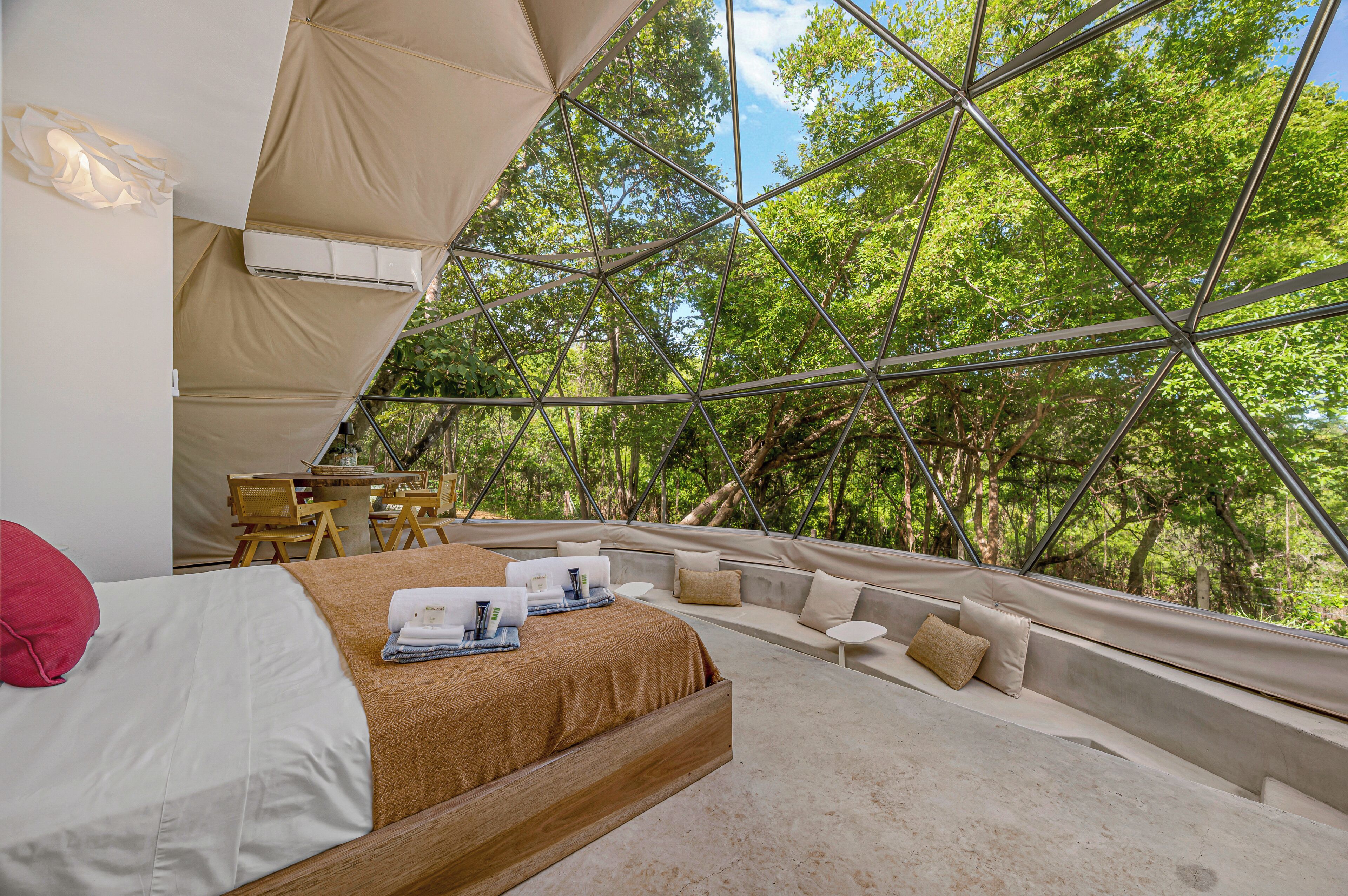 A tented accommodation with a bed, seating area, and a view of the forest.