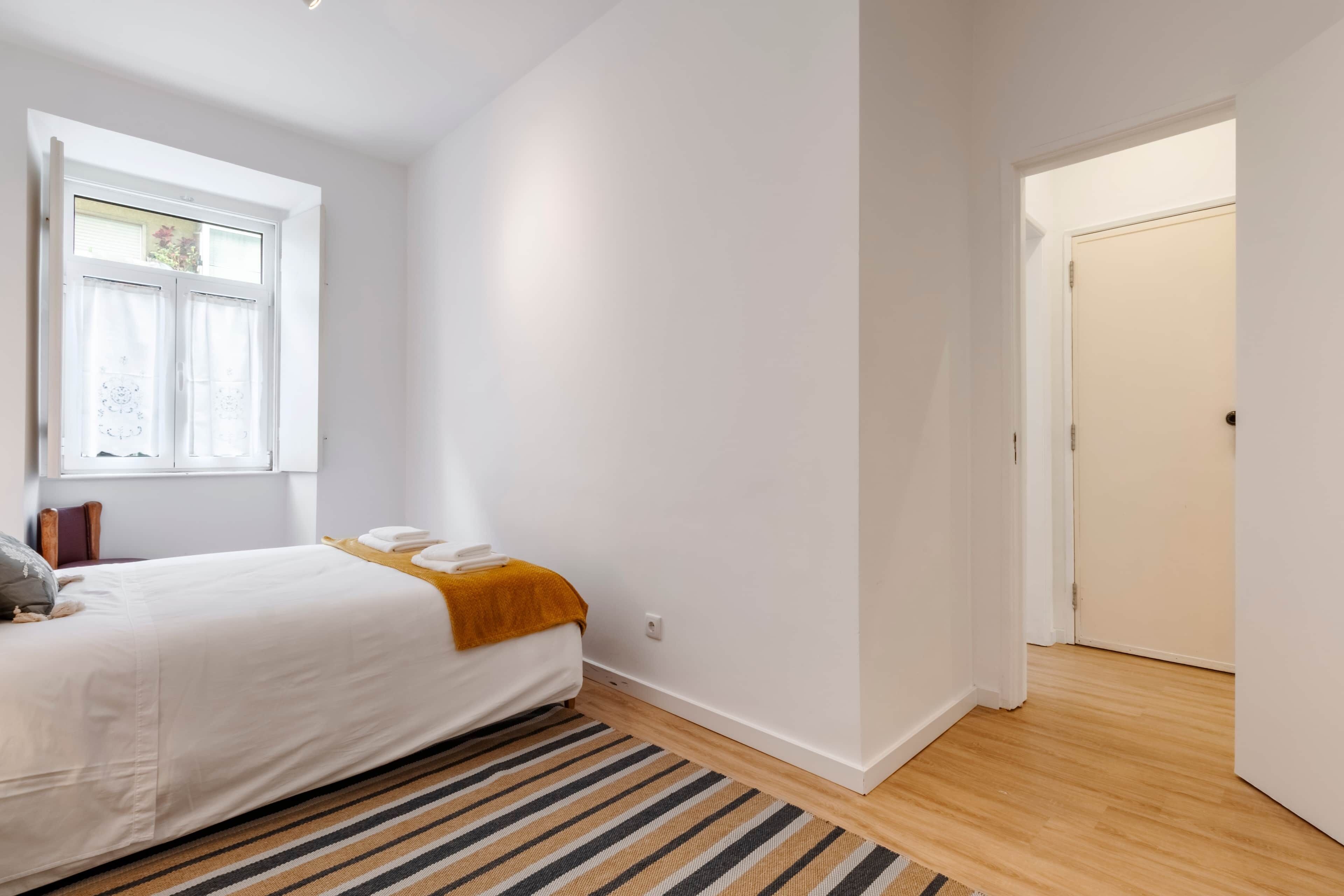 Una camera da letto con un letto, una finestra, una porta e un tappeto a righe.