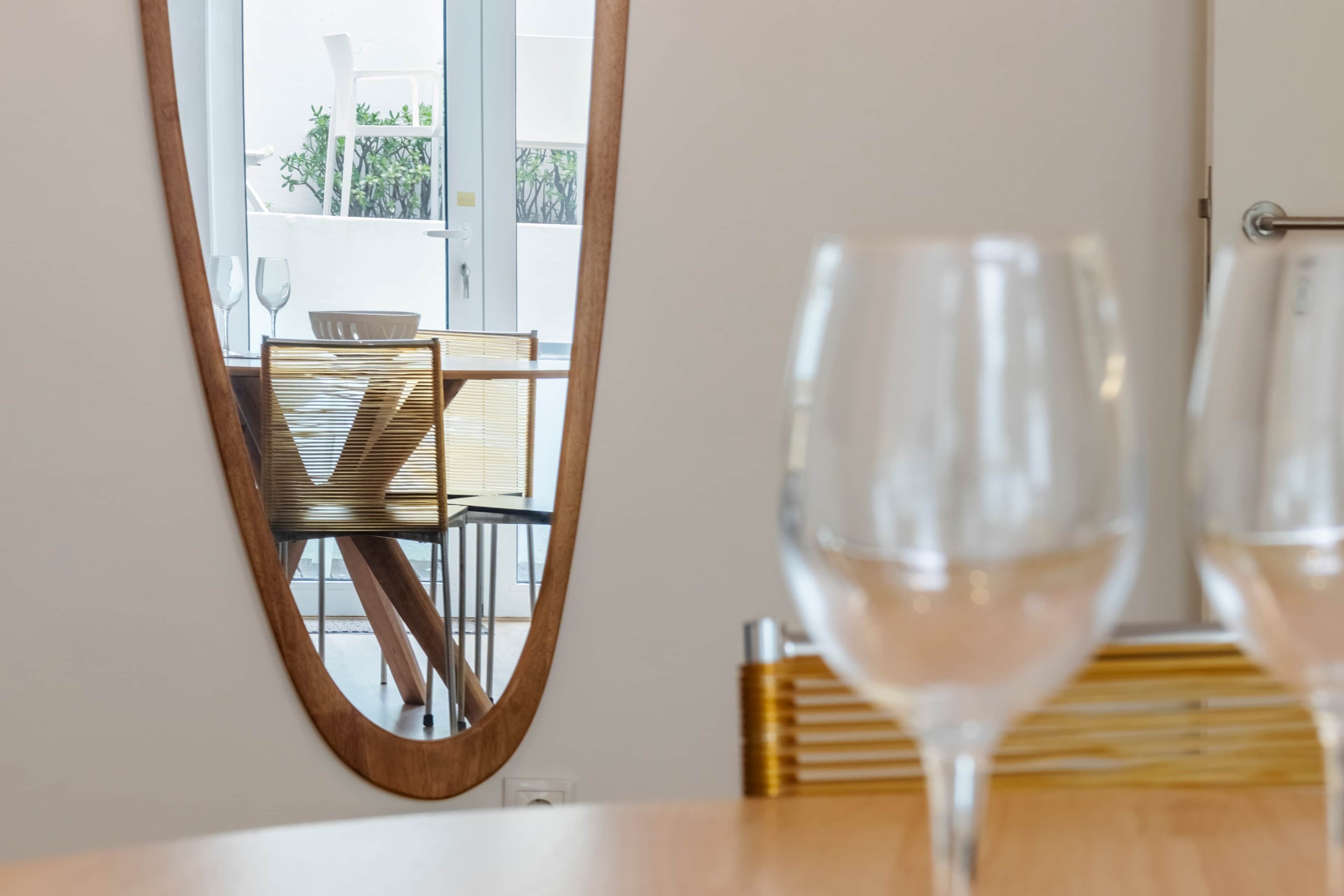 A dining area with a wooden table, chairs, and a mirror reflecting the space.