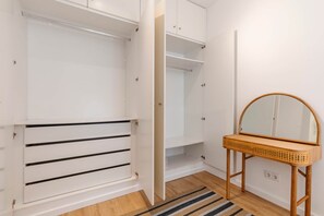 Een inloopkast met open deuren, een spiegel op een houten standaard, en een gestreept vloerkleed.