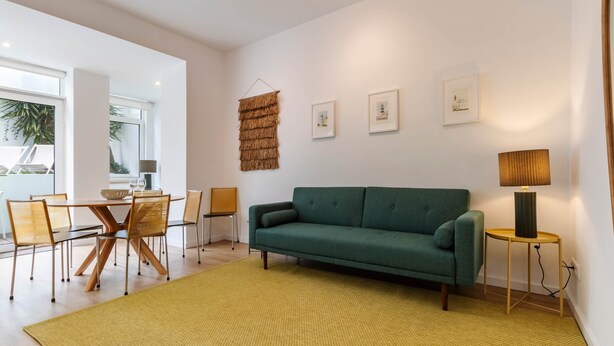 En moderne stue med en grøn sofa, et spisebord med stole og en gul løber.